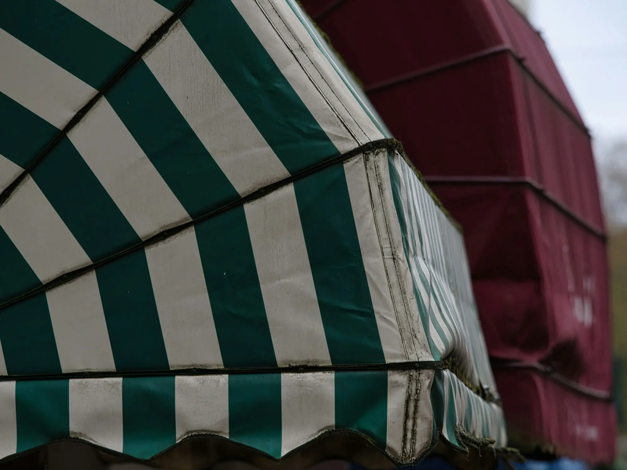 Green and white striped stall awning beside a maroon canopy at a trader market